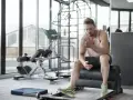 Hombre sentado en un banco de gimnasio, reflexionando sobre cuanto descansar entre series.