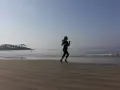 Mujer corriendo en la playa al amanecer, con el mar y una isla con palmeras al fondo.