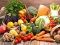 Variedad de tipos de verdura y frutas frescas sobre mesa de madera: brócoli, coliflor, zanahorias, tomates, repollo morado, peras, manzanas, plátanos, limones, jengibre y patatas.