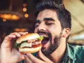 Hombre disfrutando un jugoso **cheat meal** de hamburguesa, con los ojos cerrados por el placer.