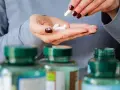 Manos con uñas oscuras sostienen pastillas blancas. Se ven frascos de suplementos. Descubre los beneficios del magnesio en el hombre.
