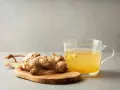 Raíz de jengibre en tabla de madera junto a una taza de té de jengibre, destacando sus propiedades beneficiosas.