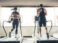 Hombre y mujer corriendo en cintas de correr, disfrutando de su rutina de cardio en ayunas.