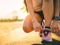 Persona se agacha para atarse los cordones de sus zapatillas rosas, lista para salir a correr al amanecer.