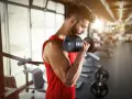 Hombre con barba entrenando bíceps con mancuerna en gimnasio. ¿Cuál es la mejor hora para entrenar?