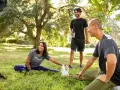 Un grupo de amigos hace estiramientos en un parque. Uno de ellos, que bebe un batido, bromea diciendo que "la creatina engorda", pero todos se ríen y siguen entrenando.