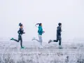 Tres personas corren en un paisaje nevado con ropa para correr en invierno.