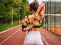 Mujer con cuerpo tonificado estirando el brazo sobre la cabeza en una pista de atletismo.
