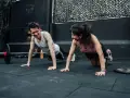 Pareja sonríe haciendo flexiones, un ejemplo de cuales son los ejercicios de fuerza.