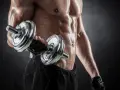 Hombre sudoroso entrenando bíceps con mancuerna. Descubre cuántas repeticiones hacer para ganar masa muscular y optimizar tu entrenamiento.