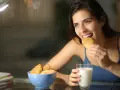 Mujer sonríe mientras come un croissant, pensando en qué picar entre horas que no engorde.