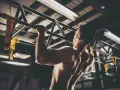 Hombre musculoso realizando pull ups en un gimnasio. Sus brazos y espalda están tensos mientras se eleva.