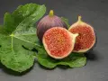 Dos higos morados, uno entero y otro partido por la mitad, reposan sobre hojas verdes y húmedas. ¡Qué delicia, los higos engordan!