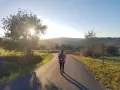 Una peregrina con mochila rosa camina por un sendero rural al atardecer, disfrutando del **camino de Santiago corriendo**.
