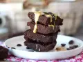 Apilados trozos de brownie de proteína cubiertos con salsa de caramelo y chispas de chocolate.