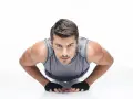 Hombre concentrado haciendo diamond push ups, con guantes negros y camiseta gris.