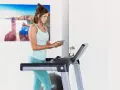 Mujer sonriente en cinta de correr, revisando su teléfono. Quizás buscando cuántas calorías debo comer al día para mantener su energía.
