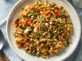 Ensalada de farro que es un plato mediterráneo con tomates secos, piñones y queso feta desmenuzado, todo mezclado con granos de farro.