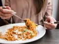 Mujer disfrutando un plato de pasta integral con salsa boloñesa y queso rallado. ¡Cuidado, la pasta integral engorda si no se consume con moderación!