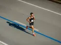 Corredor concentrado en la carrera, aprendiendo como respirar al correr para optimizar su rendimiento. Su sombra se proyecta larga sobre el asfalto.