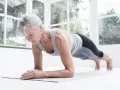 Mujer mayor haciendo plancha en su sala, demostrando que el fitness en casa es para todas las edades.