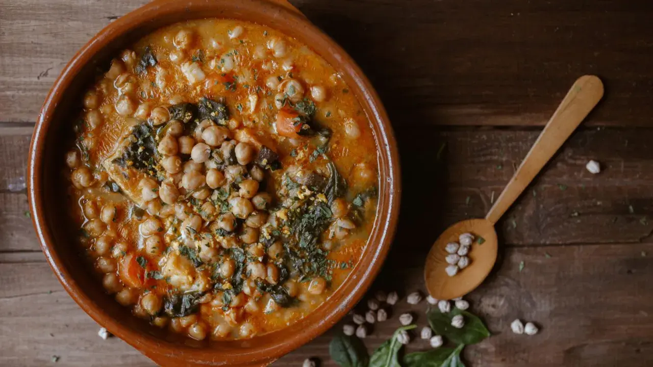 Guiso de garbanzos con espinacas y huevo, un plato rico en alimentos con hierro. Cuchara de madera con garbanzos.