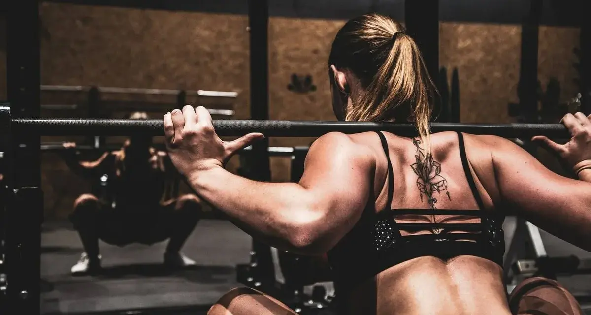 Mujer haciendo sentadillas con barra, un ejercicio clave para saber como ganar masa muscular rápido.