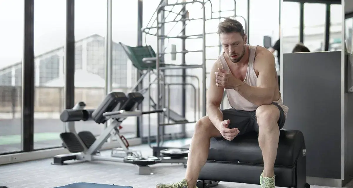 Hombre sentado en un banco de gimnasio, reflexionando sobre cuanto descansar entre series.