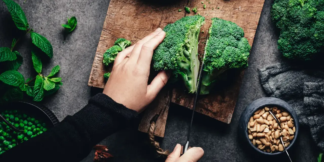 Manos cortando brócoli, un alimento rico en silicio, junto a guisantes y cacahuetes.