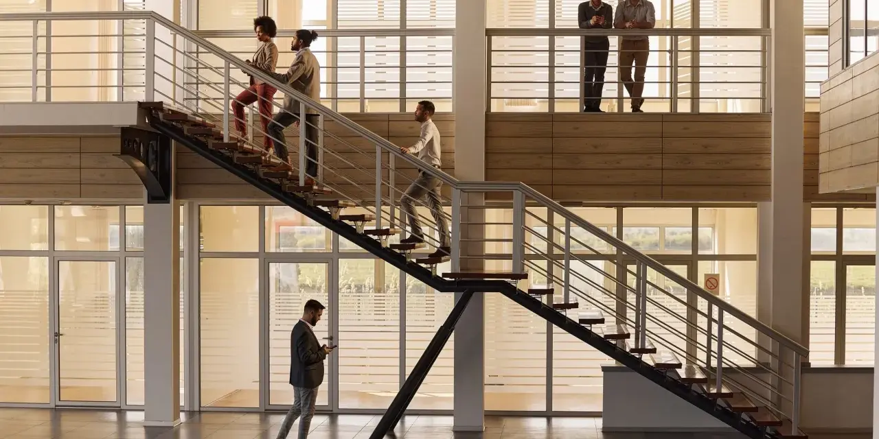 Personas subiendo escaleras, disfrutando de los beneficios de la actividad física en un moderno edificio de oficinas.