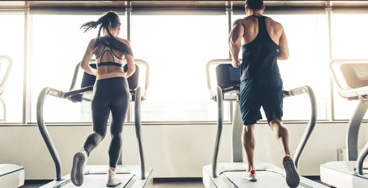 Hombre y mujer corriendo en cintas de correr, disfrutando de su rutina de cardio en ayunas.