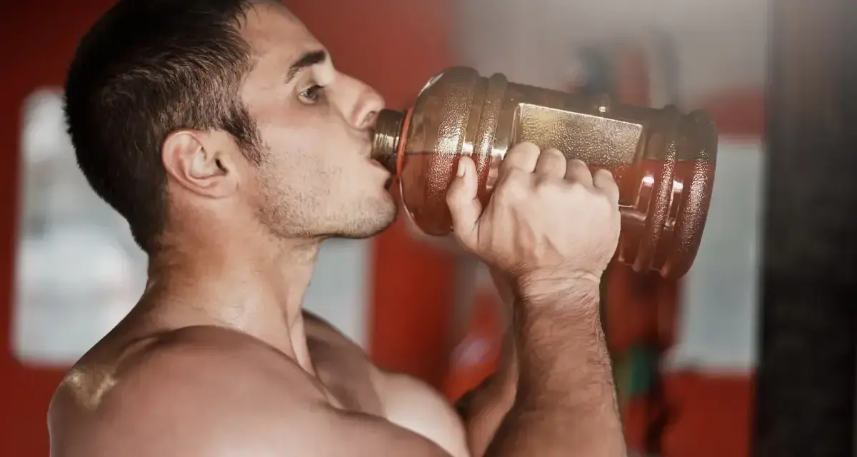 Hombre bebiendo de una botella grande, preparándose para el entrenamiento. ¿Cuántos gramos de pre entreno tomar?