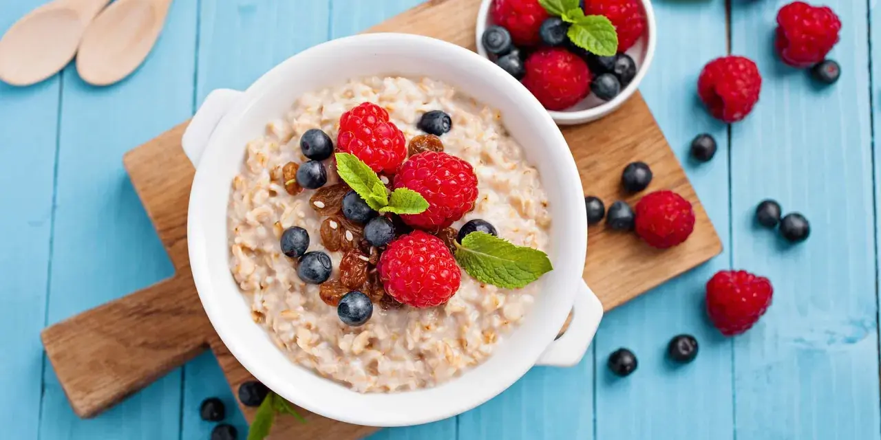 Un tazón de avena con frambuesas, arándanos y pasas. Descubre los beneficios de la avena por la noche para un descanso reparador.
