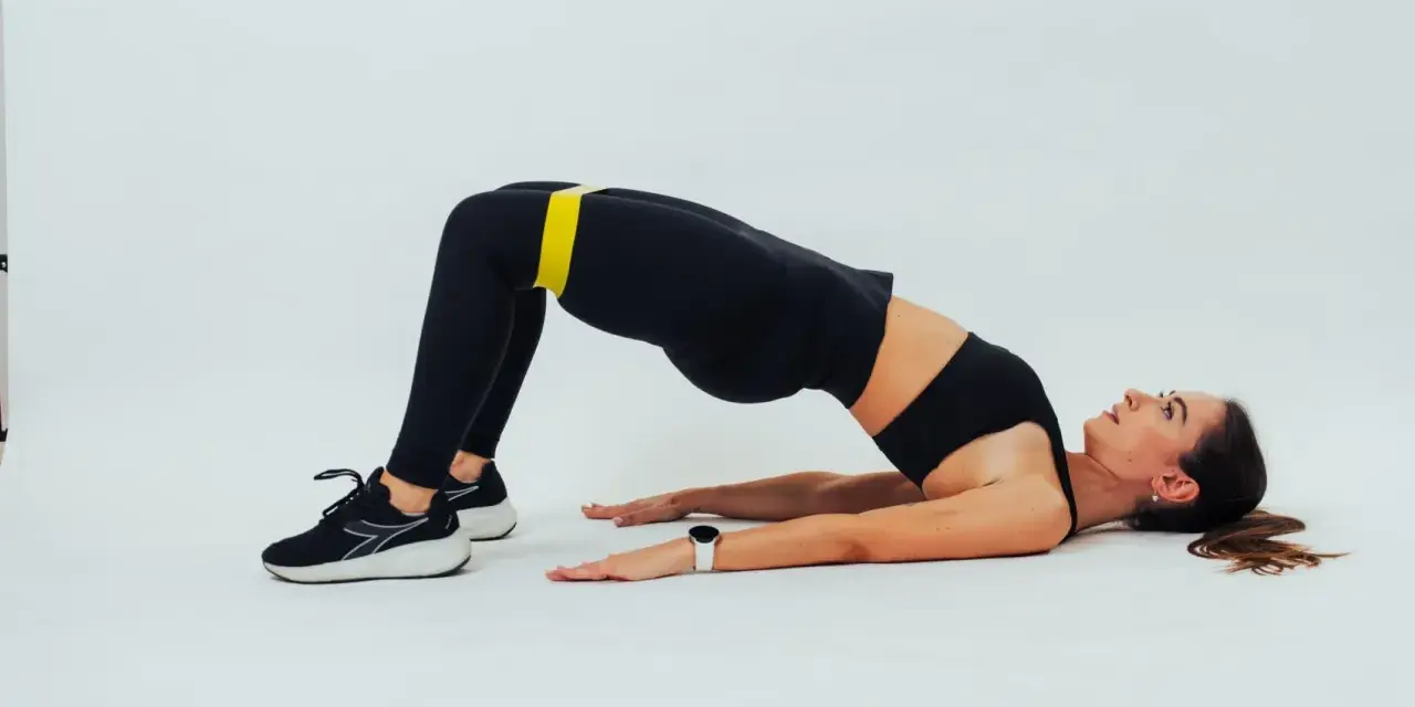 Mujer con banda amarilla en glúteos, en posición de glute bridge hold, con fondo blanco.