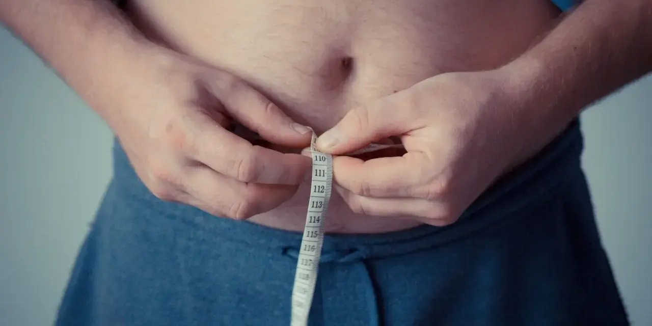 Man measuring waist with tape. A step towards understanding como activar la autofagia for better health.