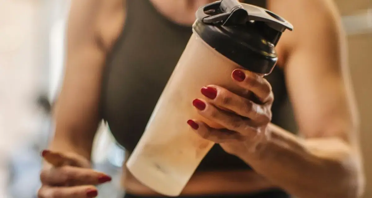 Mujer con uñas rojas sostiene un batido. ¿Los BCAA engordan? La respuesta depende de tu dieta.