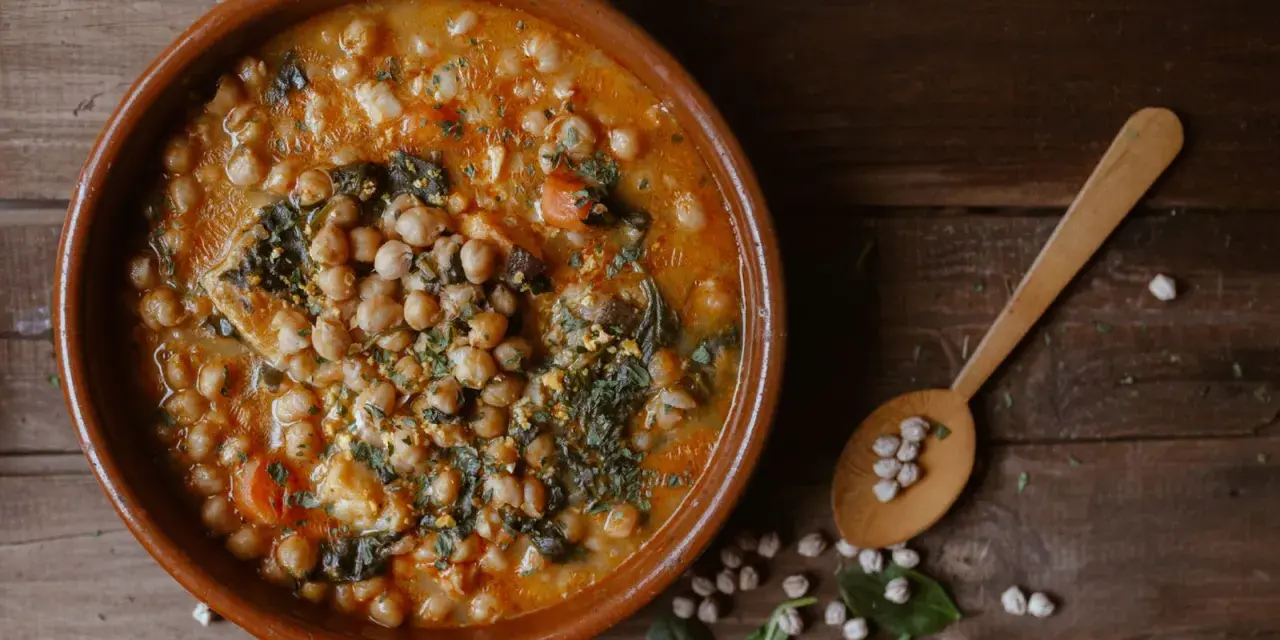 Guiso de garbanzos con espinacas y huevo, un plato rico en alimentos con hierro. Cuchara de madera con garbanzos.