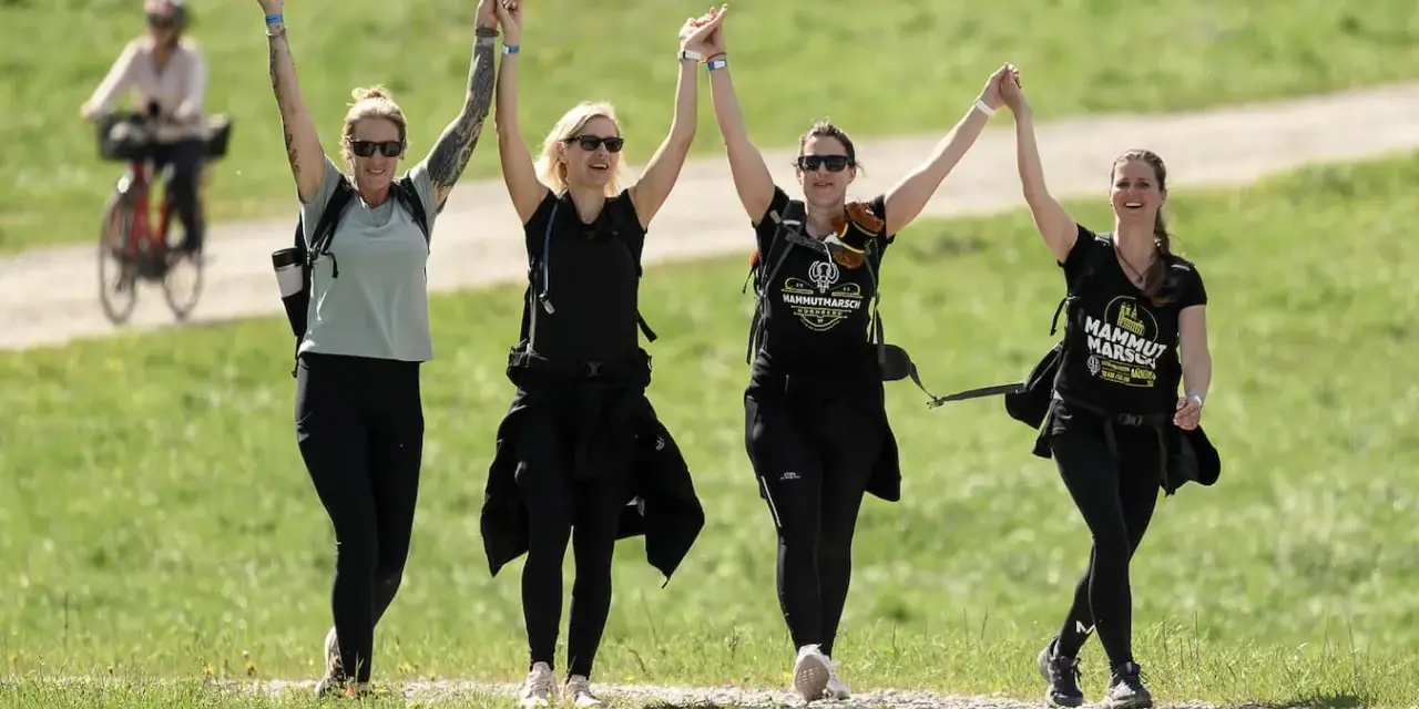 Cuatro mujeres celebran tomadas de la mano, con los brazos en alto, mientras caminan por un sendero. Su **velocidad media andando** parece alegre y enérgica.