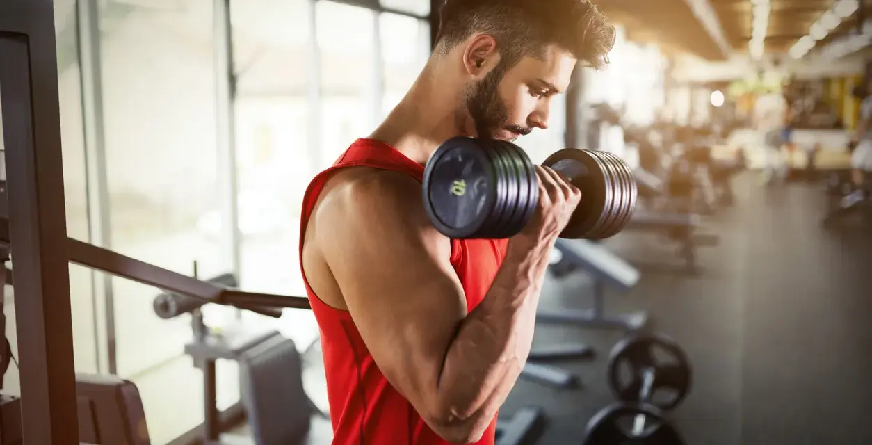 Hombre con barba entrenando bíceps con mancuerna en gimnasio. ¿Cuál es la mejor hora para entrenar?
