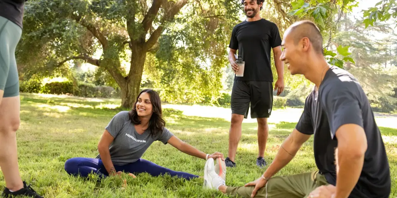 Un grupo de amigos hace estiramientos en un parque. Uno de ellos, que bebe un batido, bromea diciendo que "la creatina engorda", pero todos se ríen y siguen entrenando.