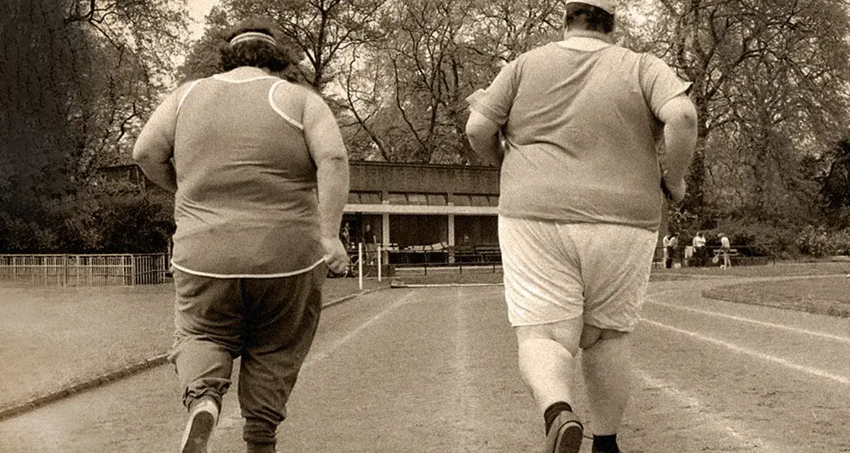 Dos personas con sobrepeso corren en una pista de atletismo. El andar adelgaza, y ellos lo saben.