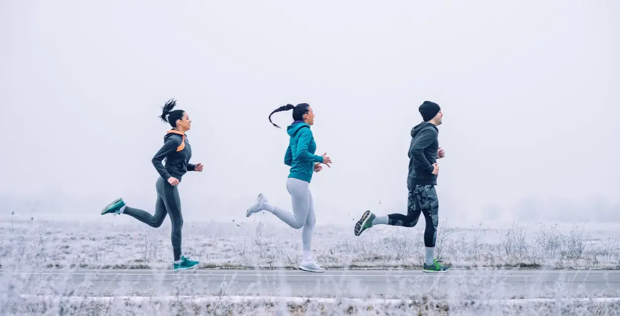 Tres personas corren en un paisaje nevado con ropa para correr en invierno.
