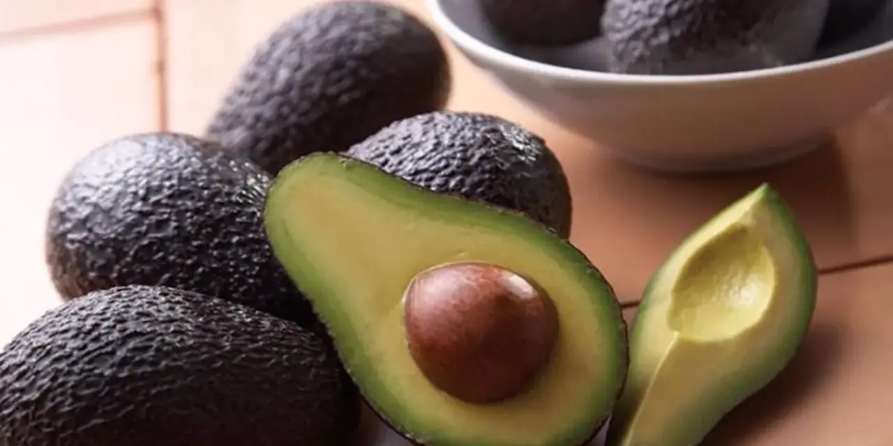 Aguacates frescos, uno cortado por la mitad mostrando su semilla, perfectos para comer aguacate todos los días y disfrutar de su cremosidad.