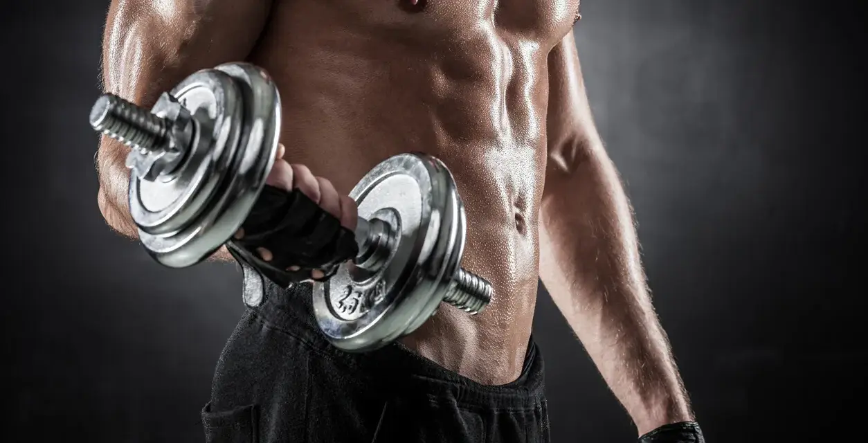 Hombre sudoroso entrenando bíceps con mancuerna. Descubre cuántas repeticiones hacer para ganar masa muscular y optimizar tu entrenamiento.