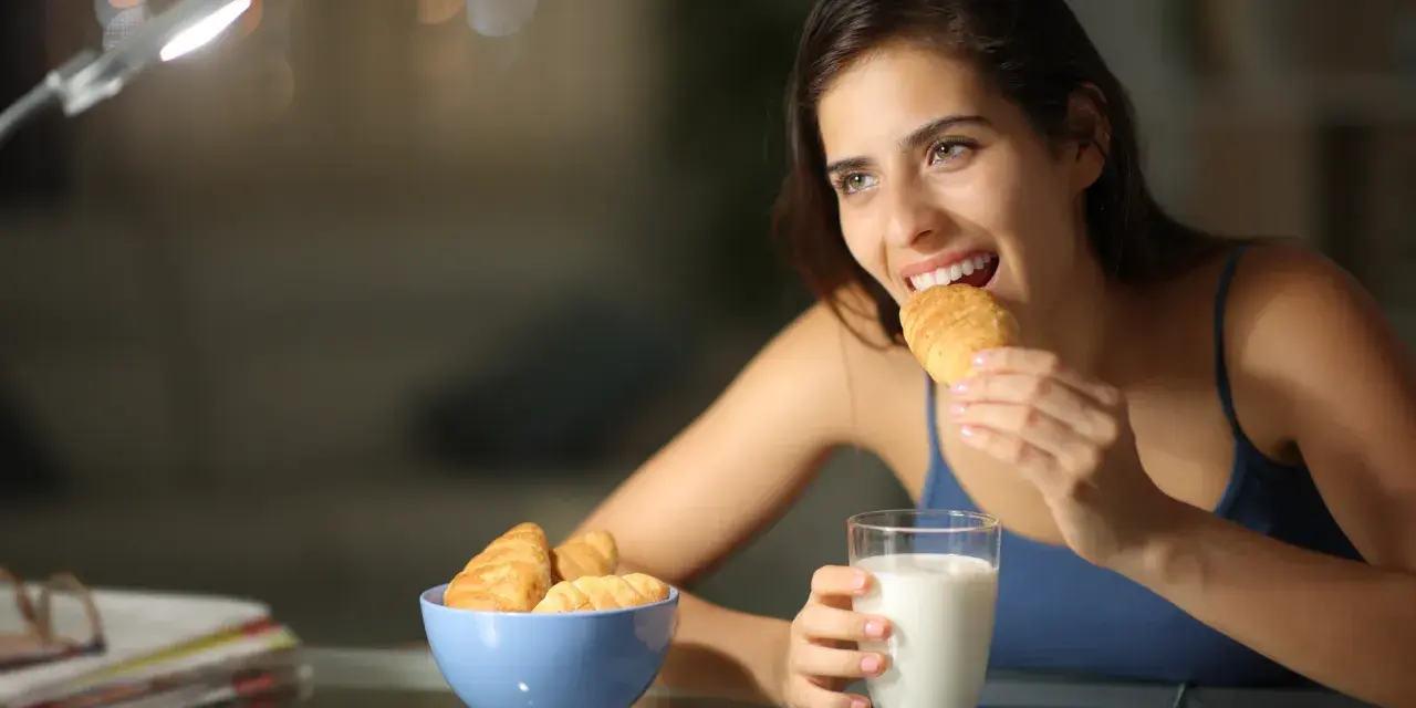 Mujer sonríe mientras come un croissant, pensando en qué picar entre horas que no engorde.