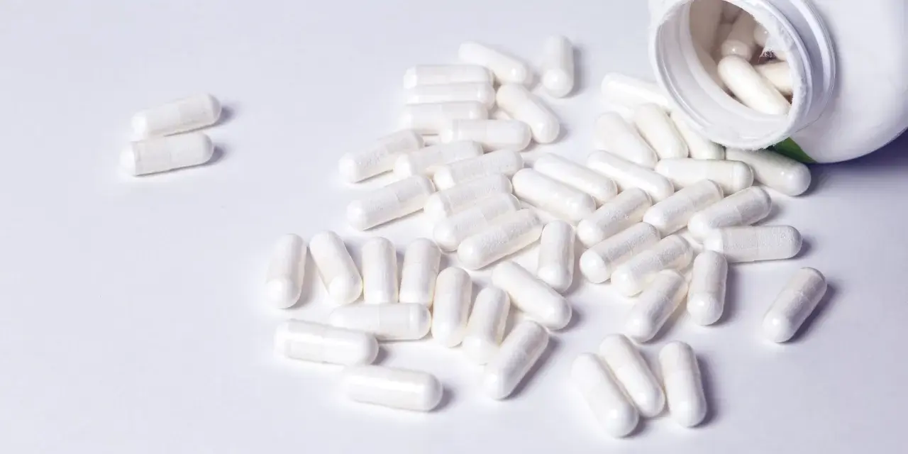 Cápsulas blancas derramadas de un frasco. Descubre para qué sirven los BCAA en mujeres y cómo pueden apoyar tu bienestar.