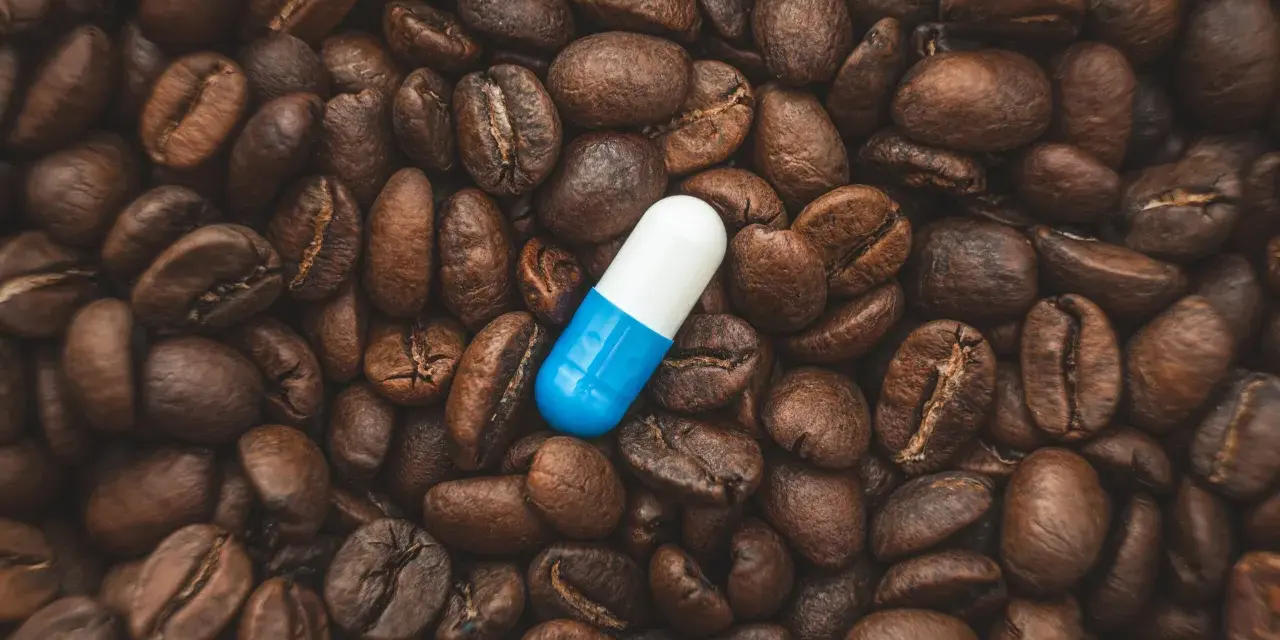Una pastilla de cafeína azul y blanca descansa sobre granos de café tostados. ¿Cuánto tarda en hacer efecto una pastilla de cafeína?