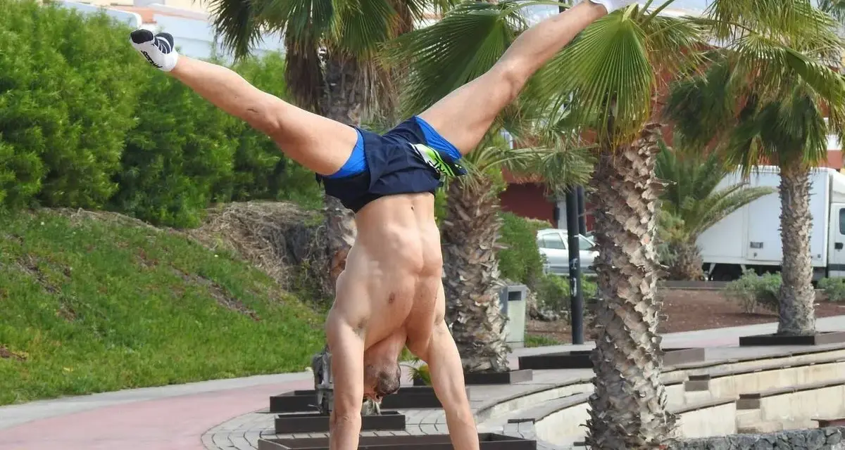 Hombre realizando ejercicios con tu propio peso, un pino en barras paralelas con palmeras de fondo.