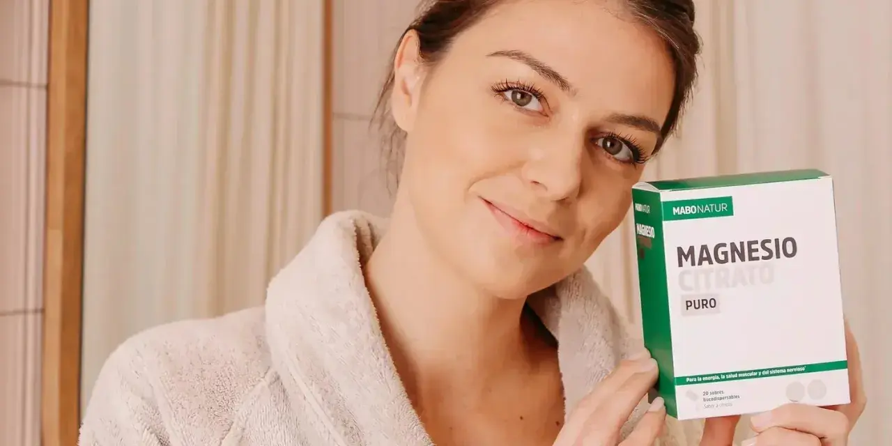 Mujer sonriente con bata, sosteniendo una caja de Magnesio Citrato Puro. Una dosis de magnesio para evitar calambres y mejorar la energía.