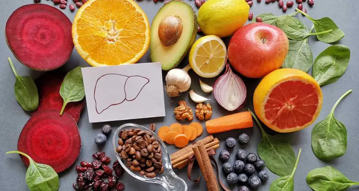 Una variedad de alimentos buenos para el hígado: remolacha, naranja, aguacate, limón, manzana, pomelo, espinacas, arándanos, café, canela, zanahoria, ajo, cebolla y nueces.